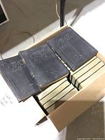 Photo showing multiple Hawkins Electrical Guides books in black embossed hardcover in a cardboard box on basement floor.