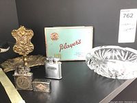 Lot showing brass ashtray, glass ashtray, Players tin, and two metal lighters.