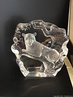 Front view of the clear crystal leopard sculpture showing carved leopard resting on a branch with detailed textures and naturalistic shape.
