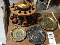 Wooden pipe holder with six assorted smoking pipes and three ashtrays arranged around on a table.