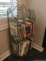 Full view of the metal decorative shelf with books on two shelves, showing scroll and leaf design.