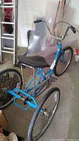 Blue adult tricycle with large saddle and three wheels, garage background
