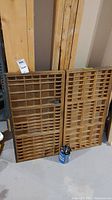 Two wooden type trays leaning against wall with tin of metal blocks at base