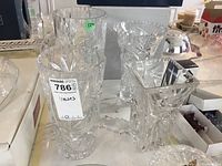 Four large clear crystal vases displayed on a marble countertop, showing varied intricate cut patterns.