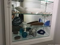 Glass display shelves showing whale figurines including a large white ceramic whale, dark marble whales, wooden puzzle whale pieces, blue glass agate slice, two geodes, and a vase with stones.