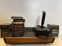 Atari 2600 console with joystick controller and stacks of game cartridges showing variety and condition.
