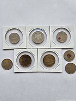 Top view of eight coins each in white cardboard holders showing obverse and reverse sides with various commemorative designs and standard coin images.