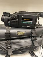 Side view of Canon Canovision 8 E310 camcorder on top of Optrex carrying case showing model name and control buttons.