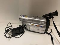 Side view of silver JVC video camera showing 700x digital zoom and digital signal processing with power adapter next to it.
