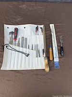 Canvas tool roll opened with multiple files, screwdrivers, wood chisels, and a scraper displayed on a brown surface.