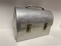 Vintage metal lunch box closed, showing the overall shape, metal build, and latches.