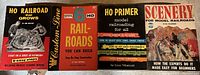 Four vintage instructional model railroad guides displayed upright showing colorful illustrated covers.