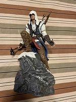Angled front view of the Assassins Creed III figurine kneeling on rock base with detailed costume and weapons.