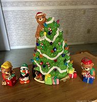 Photo of painted ceramic teddy bear Christmas tree with bears and penguin figurines arranged on wood surface