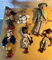 Six antique puppets and marionettes displayed on flat surface.