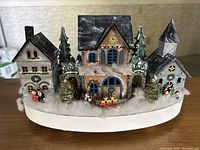 Front view of the fully assembled wooden village showing houses, clock tower, trees, painted details, and snow accents