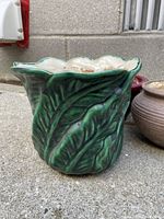 Green ceramic flower pot featuring raised leaf pattern and scalloped rim shown on concrete floor