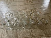 Group of 16 oz and other mason jars arranged on floor, clear glass with screw tops.