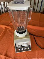 Front view of the full blender showing clear pitcher with white lid and beige base.