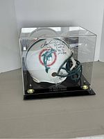 Front-left view of signed helmet in acrylic display case on black base