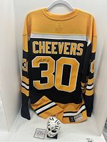 Full back view of black and gold Boston Bruins #30 jersey signed by Gary Cheevers, mask and COA at base