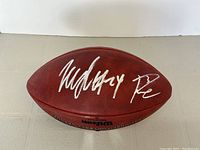 Front panel of football showing silver signatures of Marshawn Lynch and Russell Wilson on pebbled brown leather.