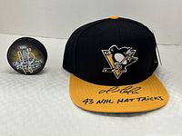 Front view showing black/gold hat and black commemorative puck side by side