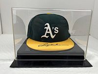 Front view of green and yellow A's cap inside acrylic case on black base showing autograph