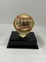 Front view of gold metallic baseball on gold glove stand with black base