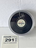 Top view of puck in clear protective case showing white autograph and Capitals logo