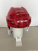 Front view of red CCM helmet on white stand with signature visible
