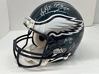 Left front three-quarter view of a dark green Philadelphia Eagles helmet with multiple silver signatures on the top and side, including player numbers.