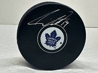 Front face of black hockey puck showing Toronto Maple Leafs logo and silver autograph