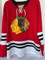 Full front view of red Chicago Blackhawks jersey with Indian head logo, lace-up collar, white and black sleeve stripes.