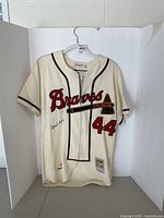 Full front view of cream jersey on hanger showing Braves script, tomahawk and number 44