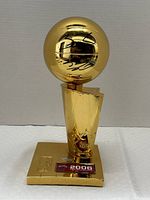 Full front view of gold-tone trophy showing sphere, base plaque marked '2006 NBA Champions' and overall design