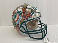 Right-side angle showing teal facemask, white shell, “9x Pro Bowl” plaque and mixed media decor.