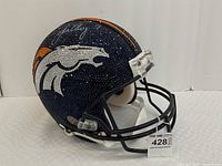Front left quarter view of full-size helmet with rhinestone-encrusted Denver Broncos logo and autograph