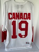 Overall rear view of white jersey showing red “CANADA” and “19” on back