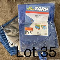 Photo shows two folded blue and silver all purpose tarps with packaging label visible for one tarp indicating 6'x8' size and features such as water resistance and aluminum grommets.