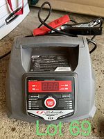 Front view of Schumacher battery charger showing digital display, buttons, and clamps attached to cables.