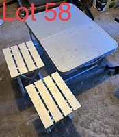 Folding camping table with two folding stools on concrete floor, showing wear and dirt marks.