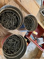 Three metal cans filled with assorted screws and nails of varying sizes, showing nails with flat heads and screws with threads.