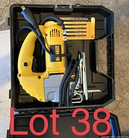 DeWalt yellow and black electric jigsaw inside open black plastic case, with coiled power cord and extra jigsaw blades in yellow packaging.