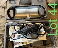 Open case revealing black Dremel rotary tool with power cord, manuals and papers inside the molded compartments.