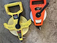 Photo of two measuring tapes: one yellow 200-foot tape with D-shaped handle, and one orange 100-foot tape with rectangular handle, both labeled 'Rogerson'.