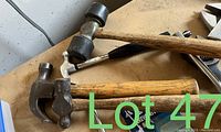 Photo showing 3 hammers of different sizes and types with wooden handles and metal heads, placed on a dusty workbench.