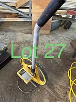 Photo shows a yellow Keson measuring wheel with a metal handle and analog counter on a concrete floor with some wood and metal objects in the background.