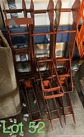 Three orange metal pump jacks arranged vertically in storage with visible wear and adjustable height sections.