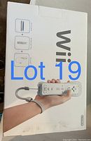 White Nintendo Wii console box with an image of a hand holding a Wii Remote Plus controller with wrist strap, showing the remote and nunchuk controller illustration on the box.